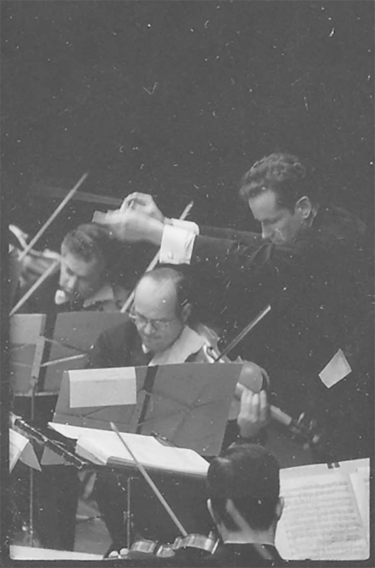 A youthful Louis Lane conducts the Orchestra. Everyone wears a serious, intense expression.