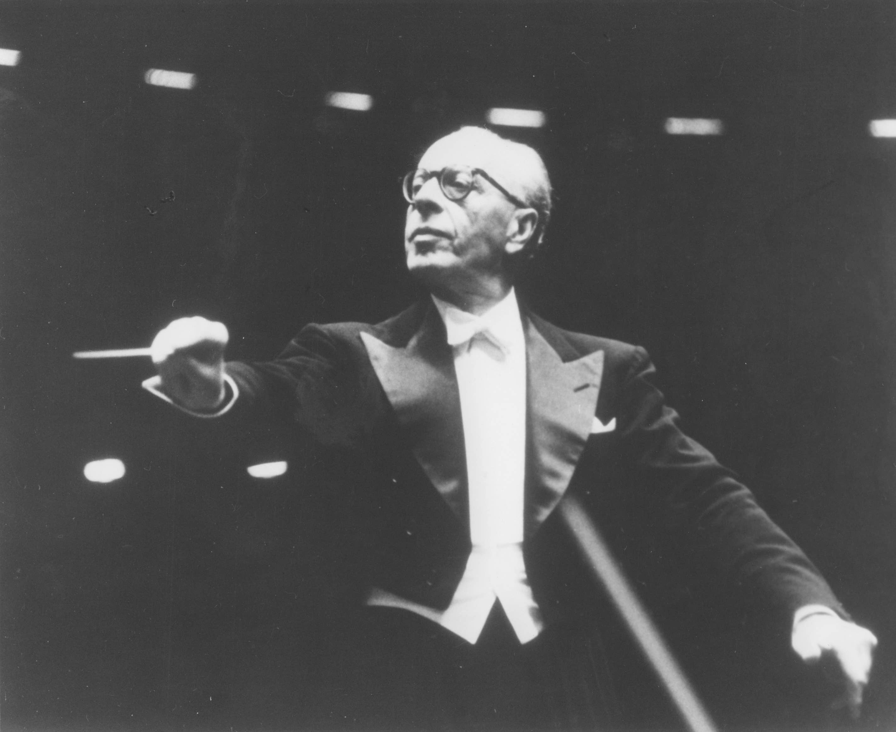 George Szell is conducting. He is looking to the left with a severe expression, and is dramatically cueing a performer.
