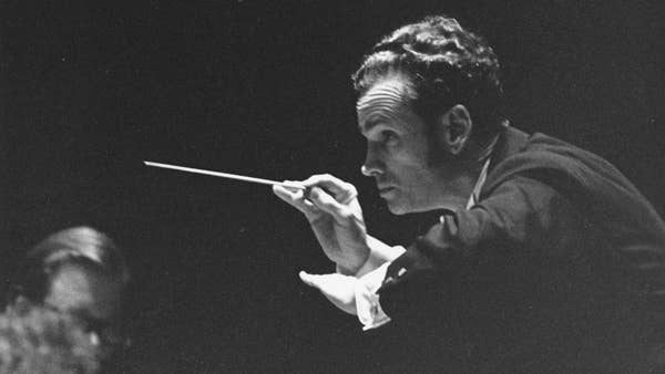 A close-up of Louis Lane conducting a concert at Severance Hall. He is bent forward slightly and gesturing to the players to play softly.