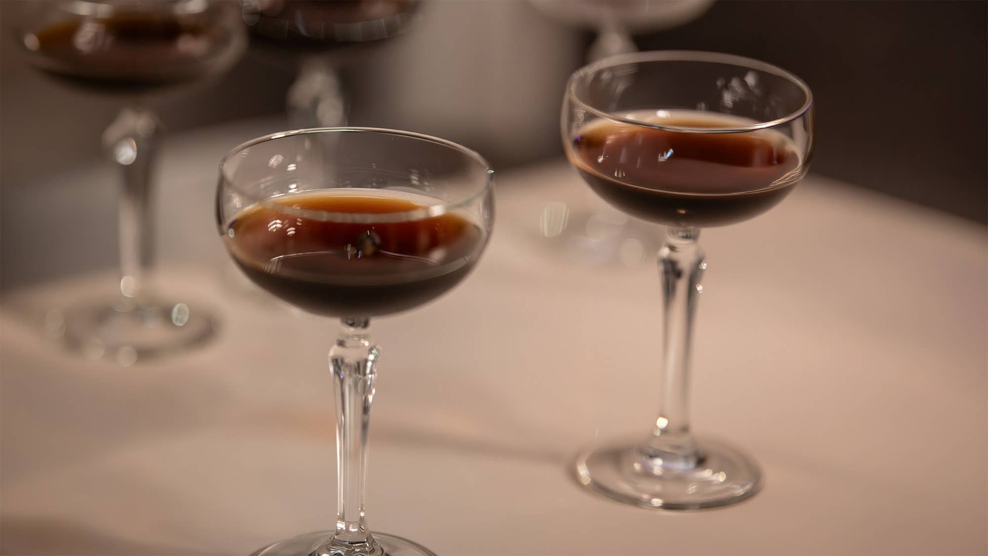 Close-up of a stemmed glass with amber-red wine, background blurred with a person serving another drink