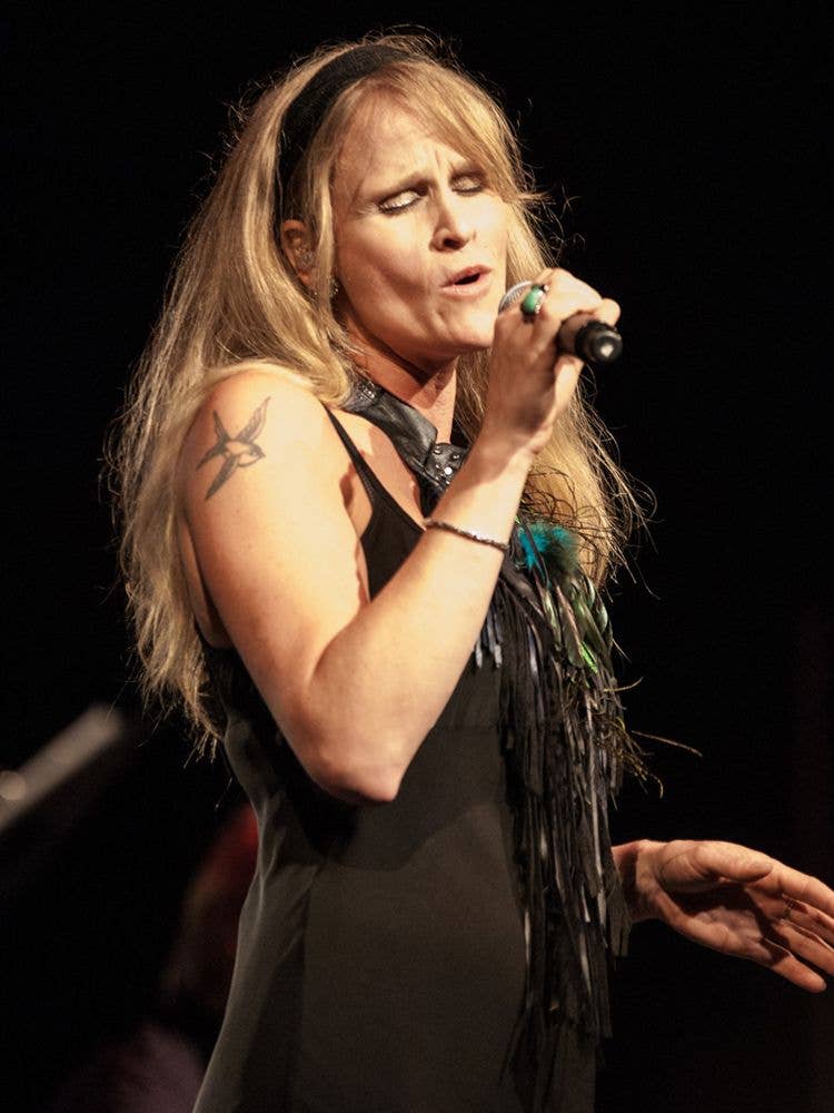 Blonde singer Andrea Koziol performs onstage, eyes closed, holding a microphone against a dark background