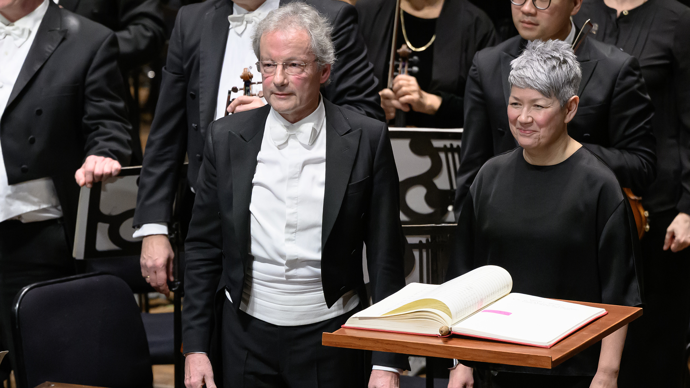 A man in a tuxedo and a woman in black smile behind a podium