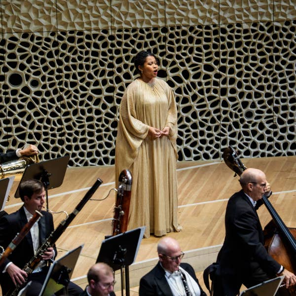 A woman in a gold dress sings behind an orchestra