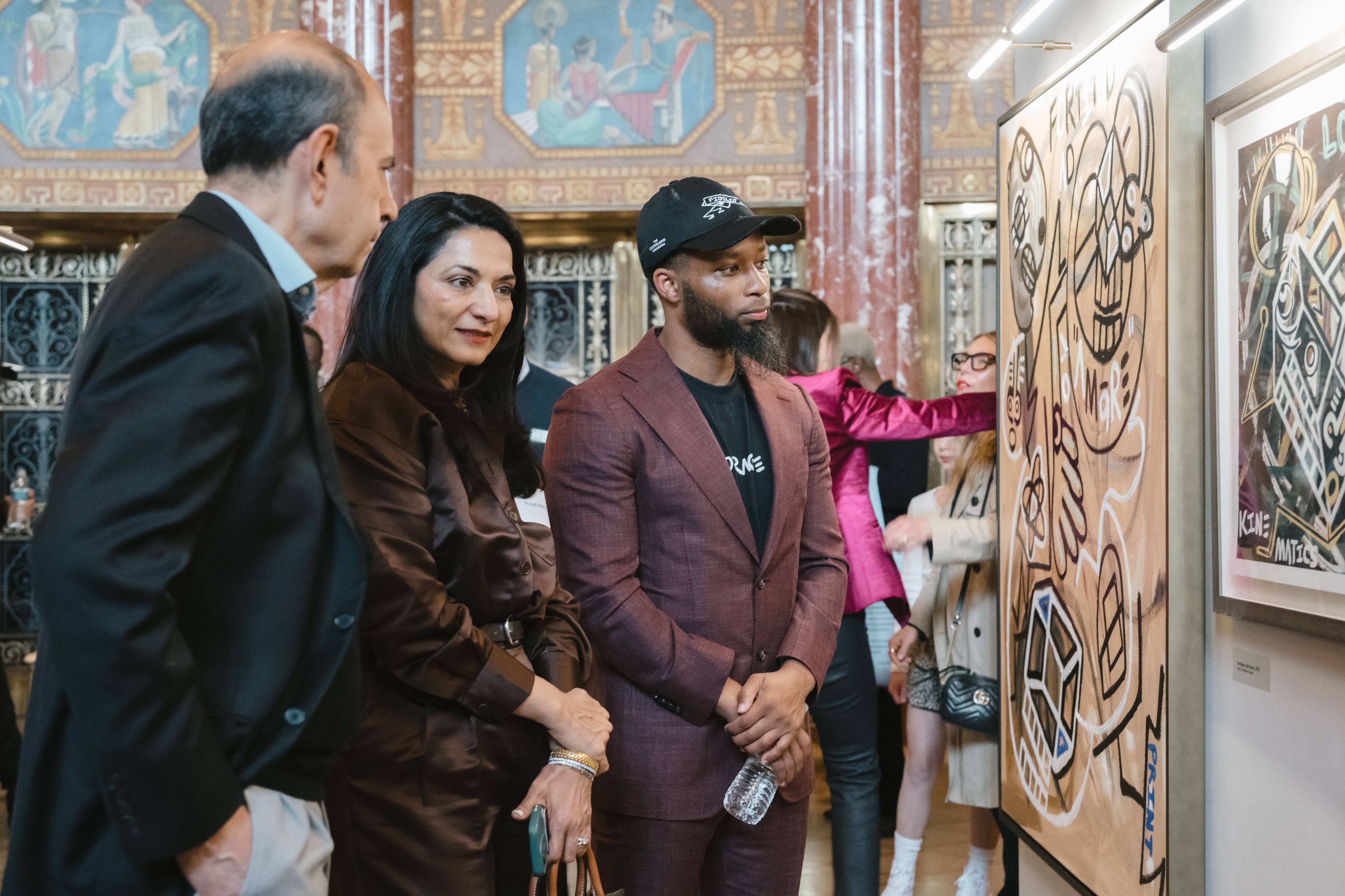A man and a woman stand near artist, Halim Flowers, viewing graffiti artwork in the Grand Foyer