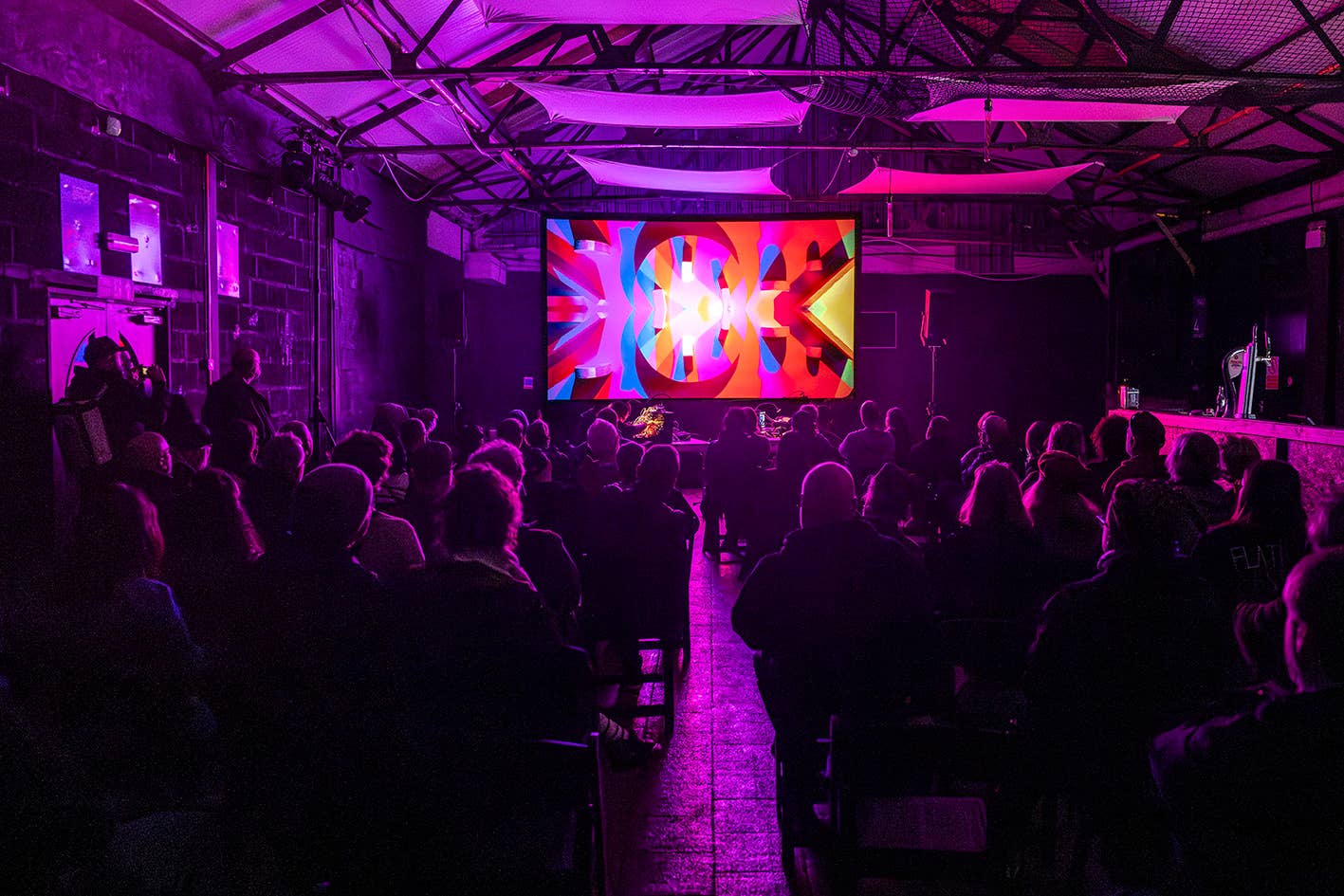 An audiovisual event from Flatpack 2026 - an audience sat in the dark watches a screen lit with bright, colourful patterns.
