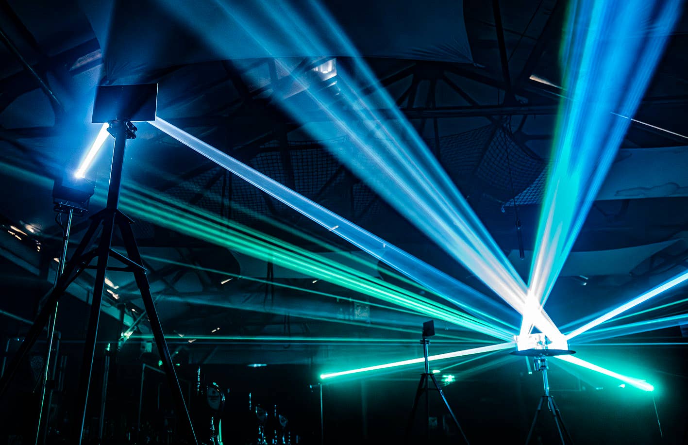 Lighting beams fan across ceiling and stage, casting blue and green laser-like light through haze