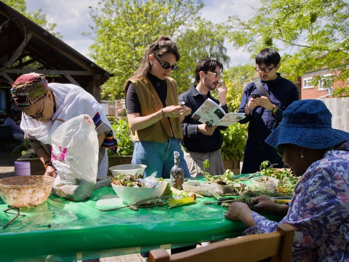 Group of people outdoors crafting at a green table in bright sunshine.