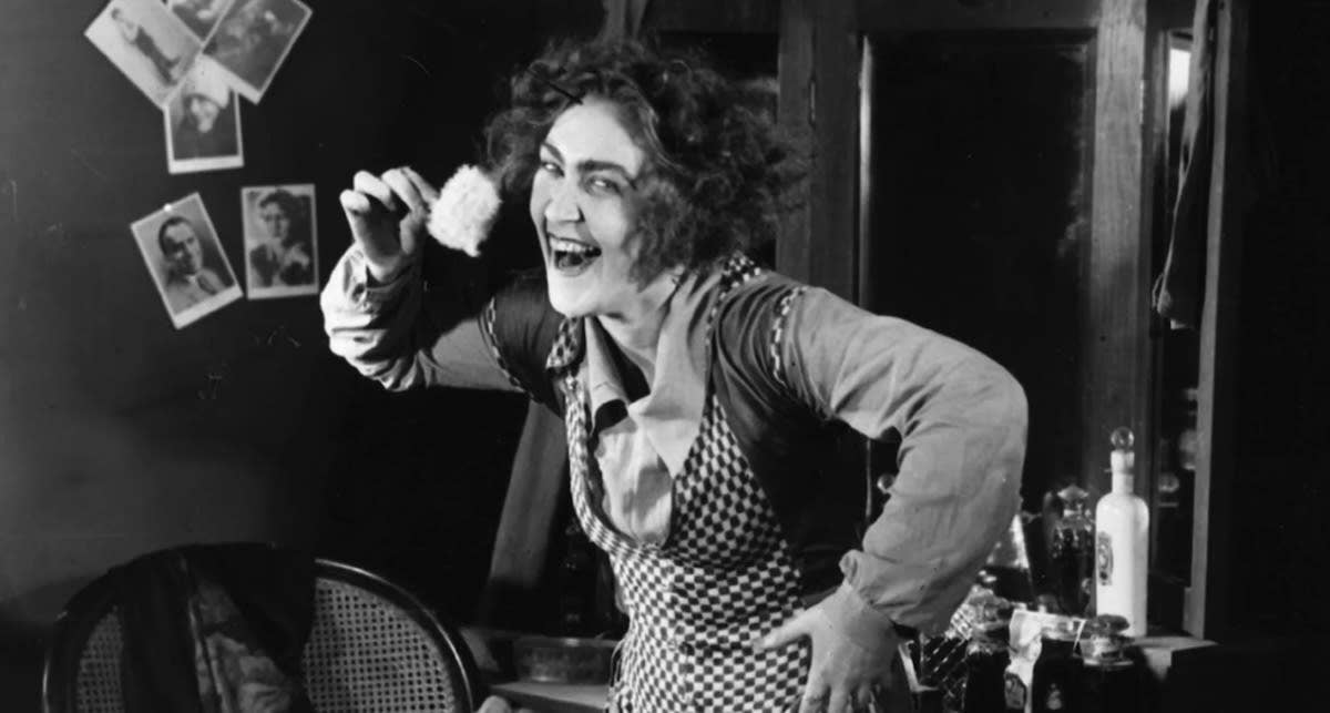 Bella Chernova as The Bureaucrat's Wife laughing open mouthed at the camera.