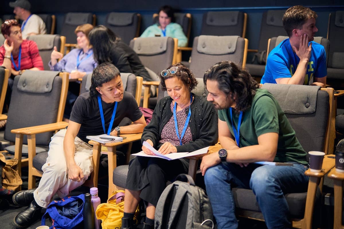Conference delegates sit in theatre seats, discussing and writing notes during the New Technologies session.