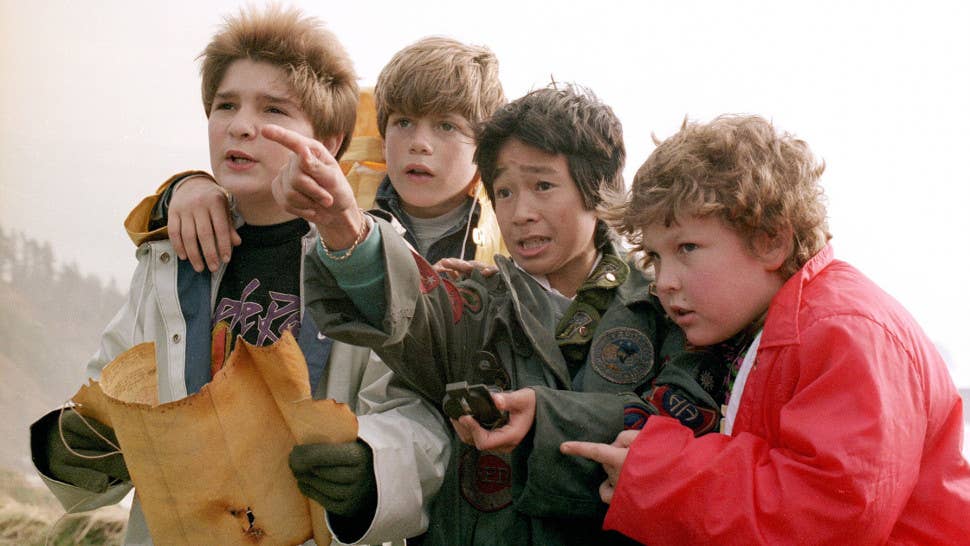Group of five boys huddle together, all looking into the distance as one boy points at something.