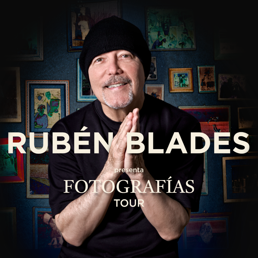 Man wearing a beanie and black shirt, hands clasped in front of a gallery wall with Spanish text overlay.