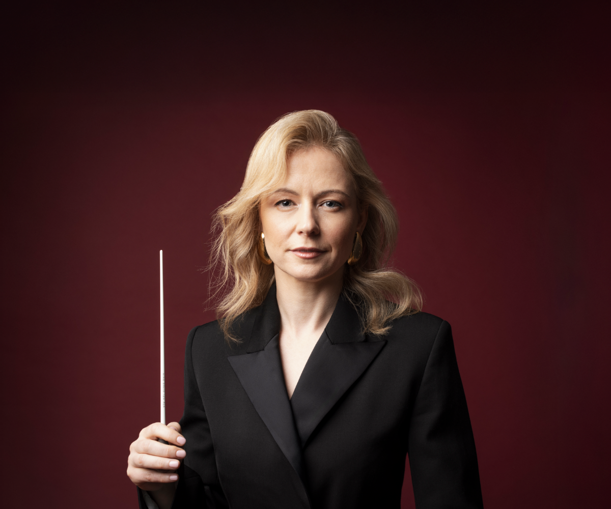 Blonde woman in a black blazer holding a baton on a deep red studio background
