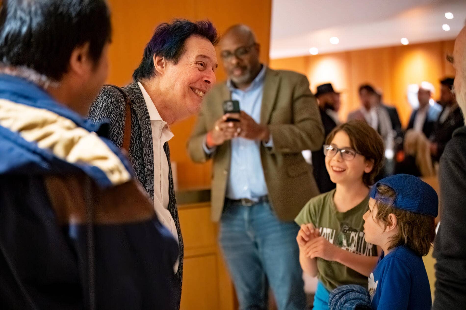 A smiling Alan Chapman chats with children at a community gathering while attendees stand in the background.