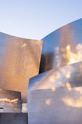 Modern museum building with curved bronze panels and skylit windows at dusk, sky background and soft reflections.
