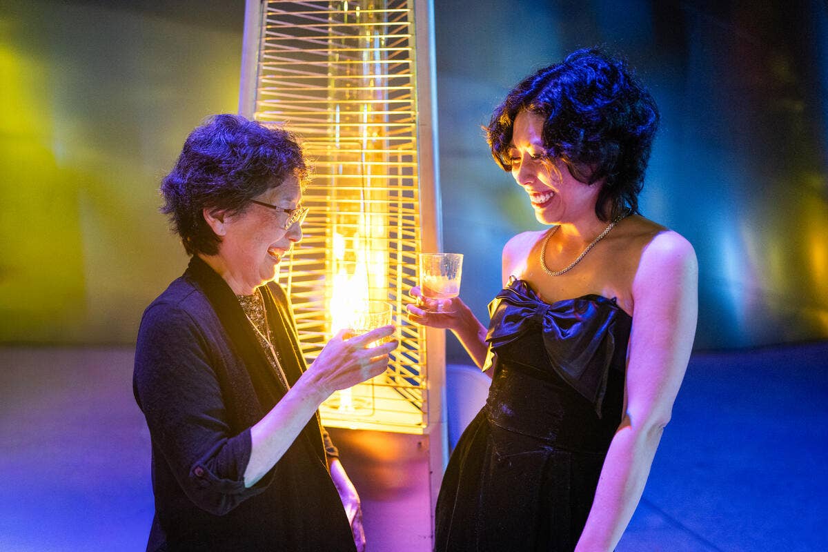 Two adults at a nighttime party, smiling and toasting with drinks beside a glowing hanging light.