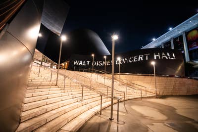 Night exterior of Walt Disney Concert Hall with illuminated facade and curved steps.