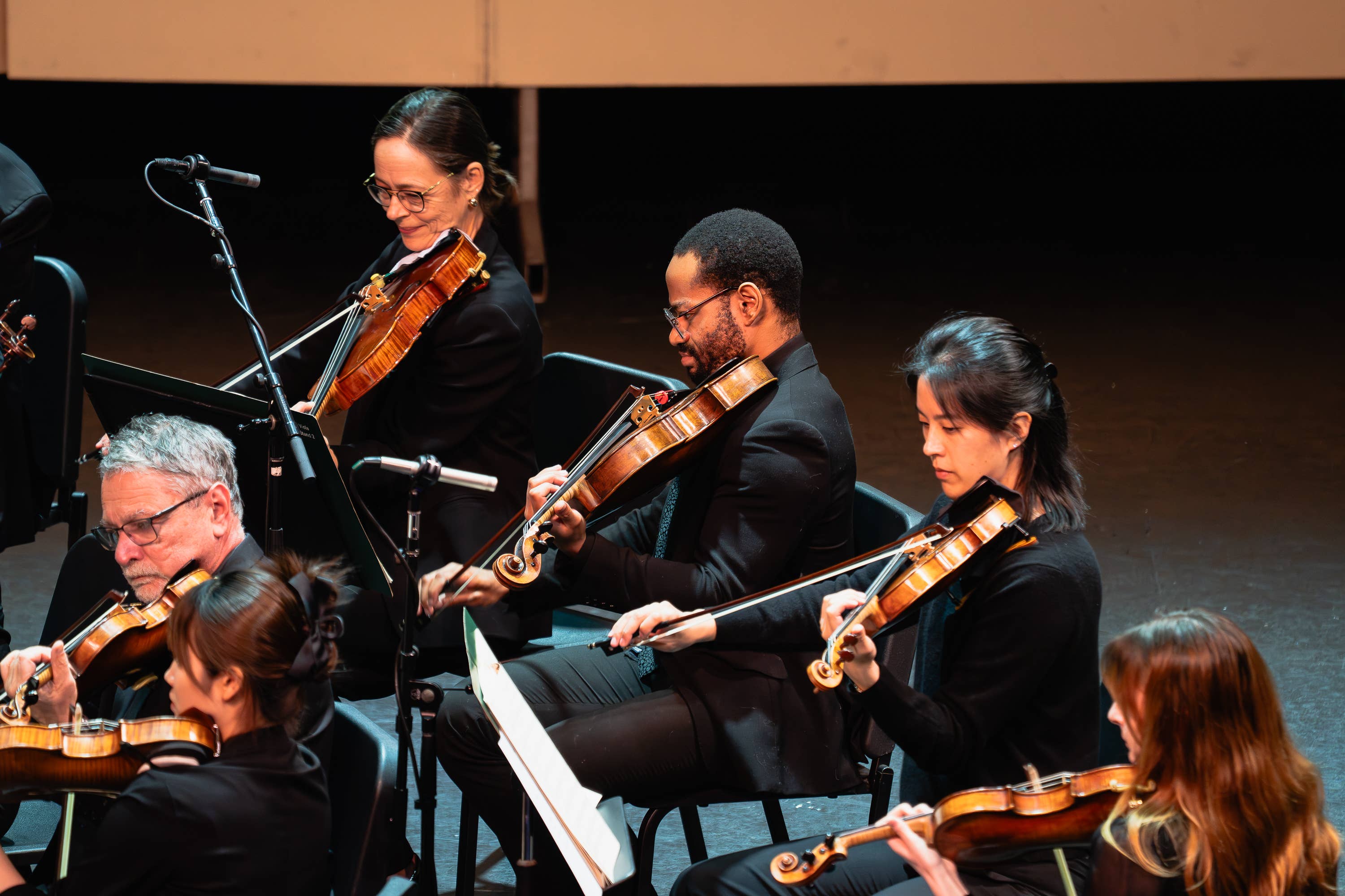 String ensemble performing on stage, with violinists and violist holding instruments in warm spotlight.
