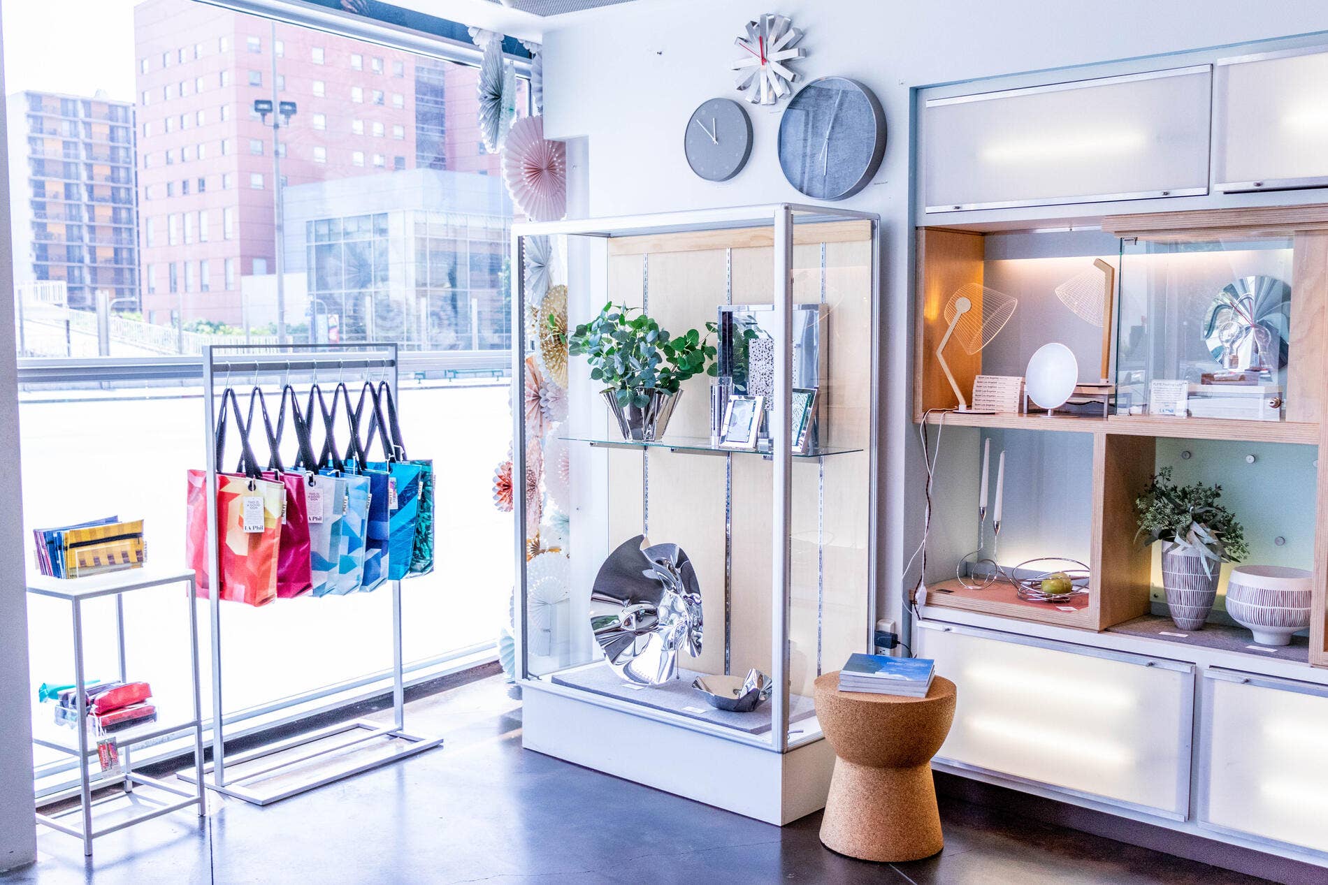 Bright retail display with gift bags, flowers, decor clocks and mirrored shelves by a window overlooking city buildings