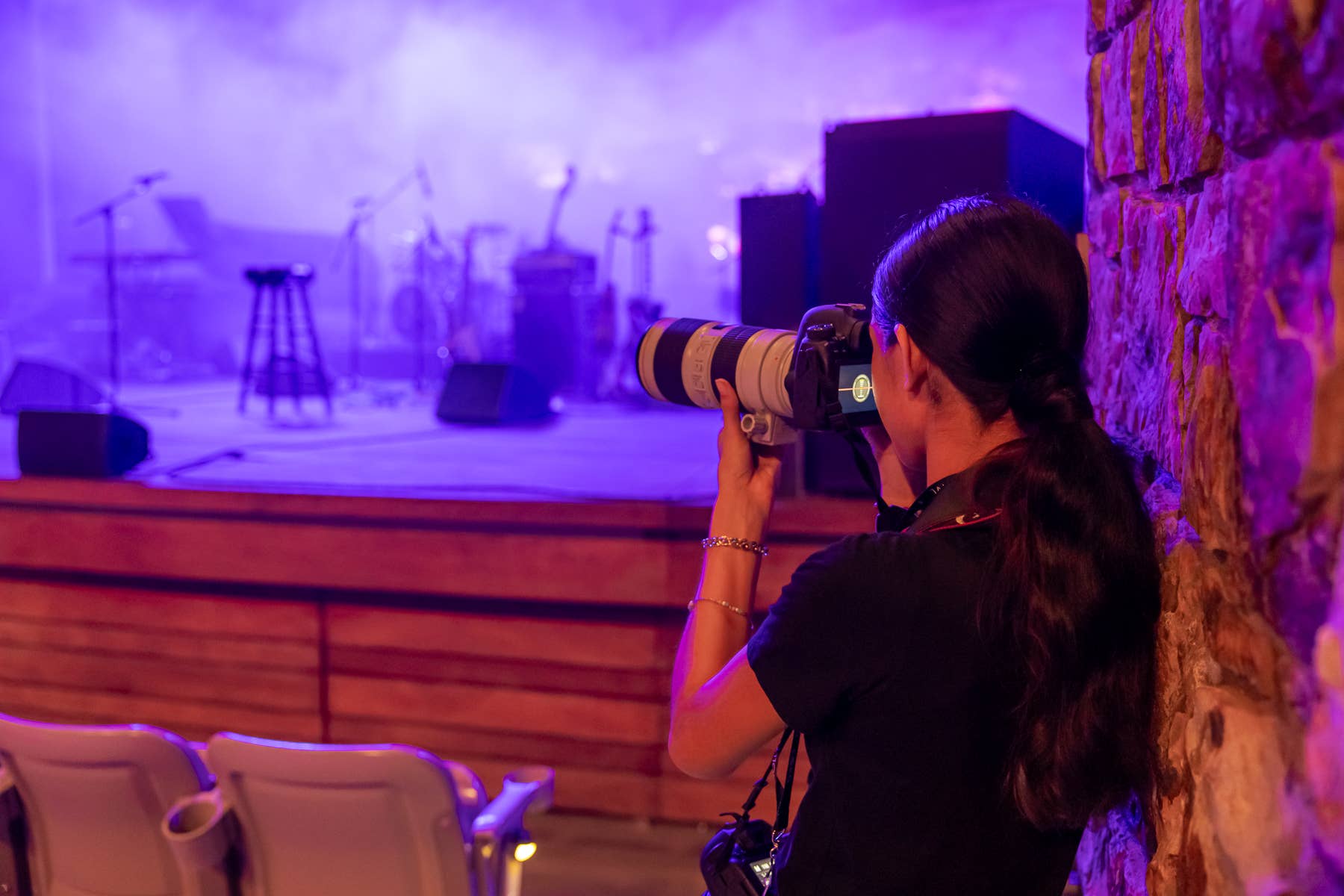 Photographer with a DSLR holding a telephoto lens, shooting a live band on stage under purple lighting