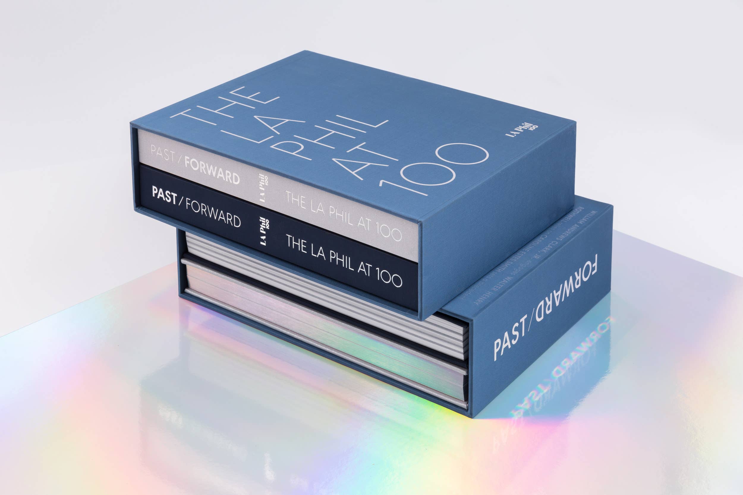 Stacked blue hardcover books with titles “Past/Forward” and “The La Phil at 100” on front and spine.