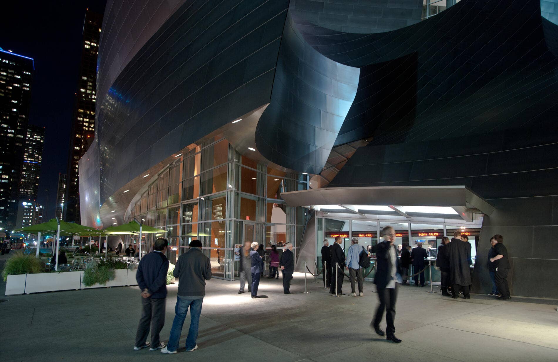 Night view of modern curved building facade with glass entrance and people lining up under streetlights