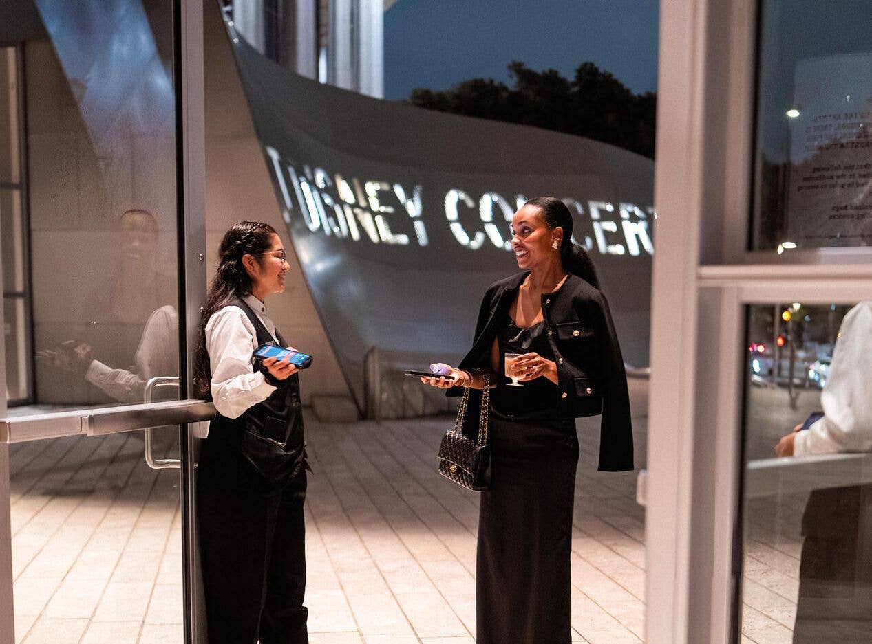 A concert hall usher welcomes in audience member at the Grand Ave entrance.