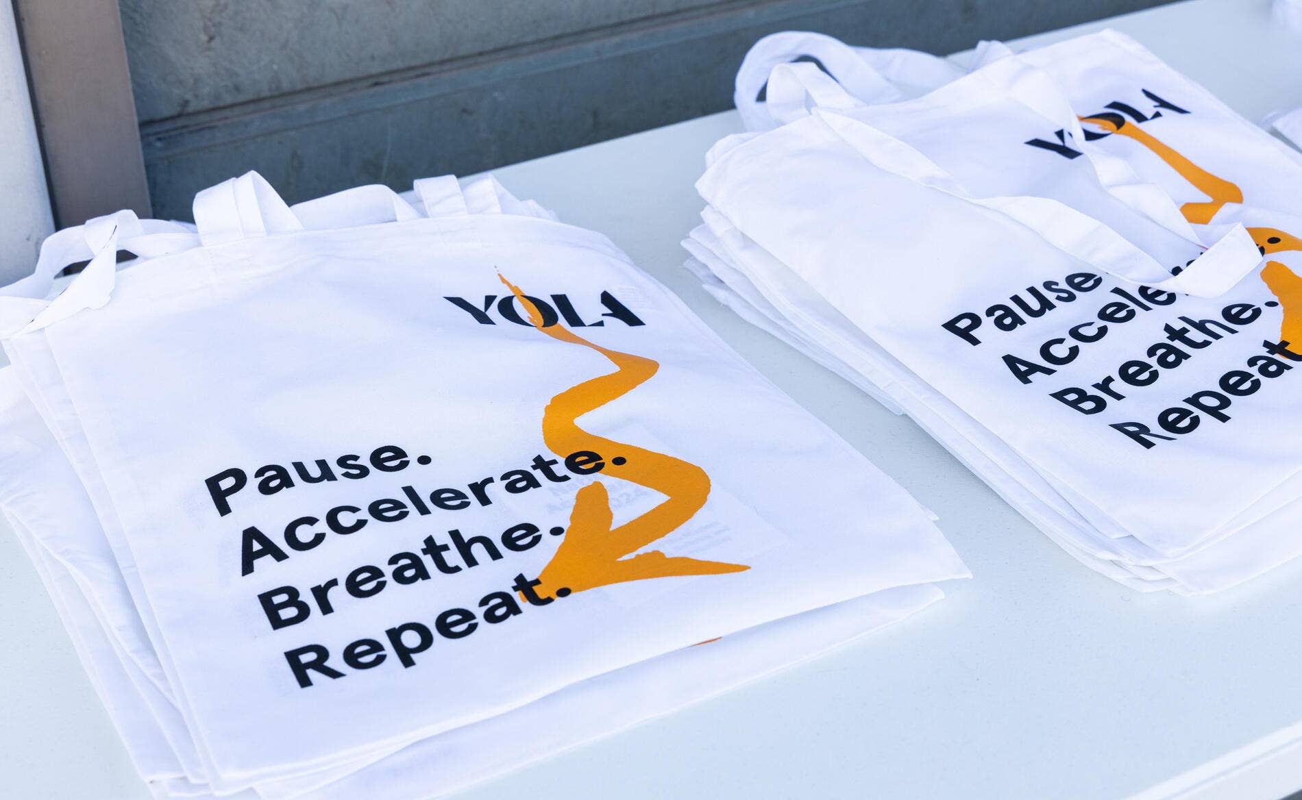 Folded white bags printed with “pause. Accelerate. Breathe.” and orange arrows, stacked in a bin.