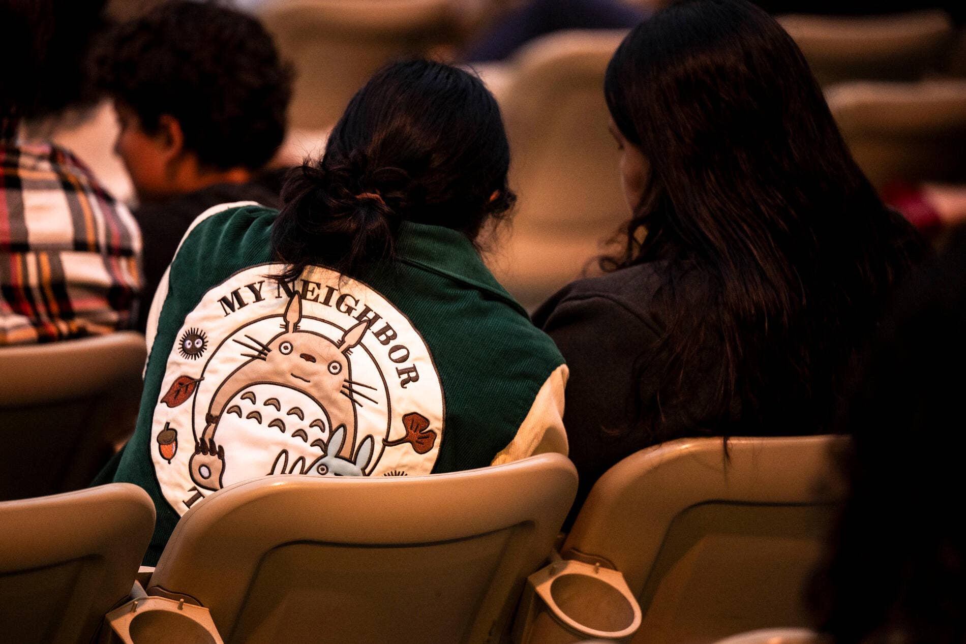 Two children sit in theater seats, backs turned, one wearing a green “My Neighbor Totoro” shirt.