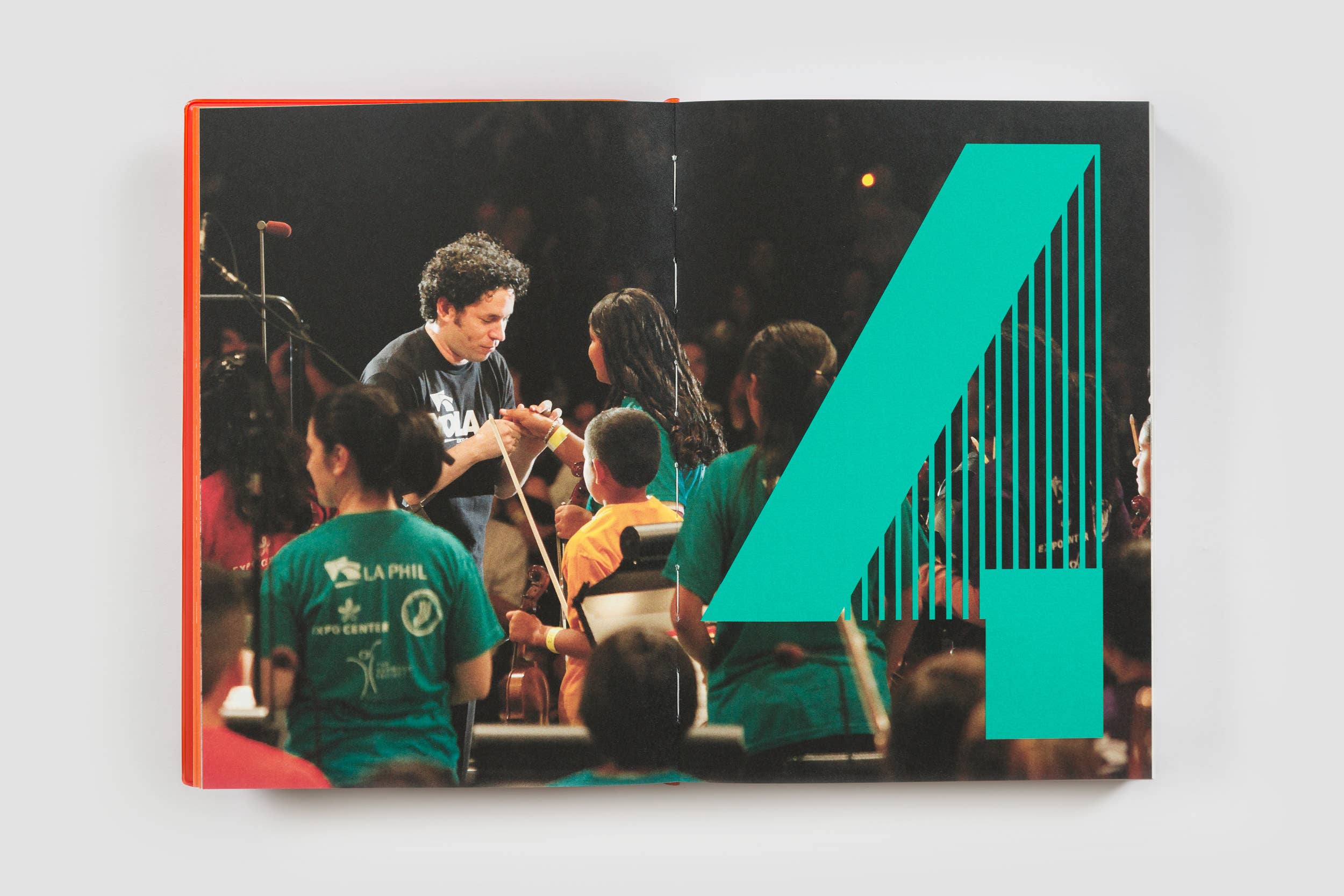 People standing in an audience as a musician and volunteers interact near a large teal graphic