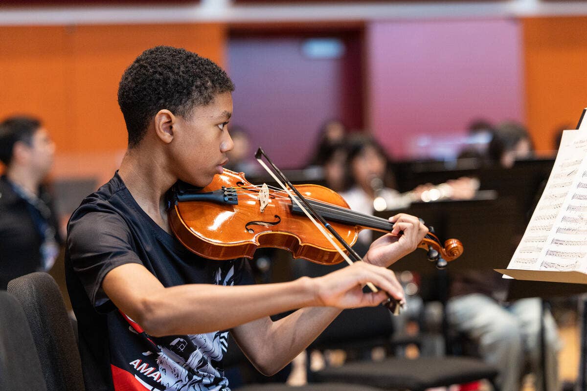 Young man playing violin in an orchestra, focused beside sheet music stand in a classroom rehearsal room