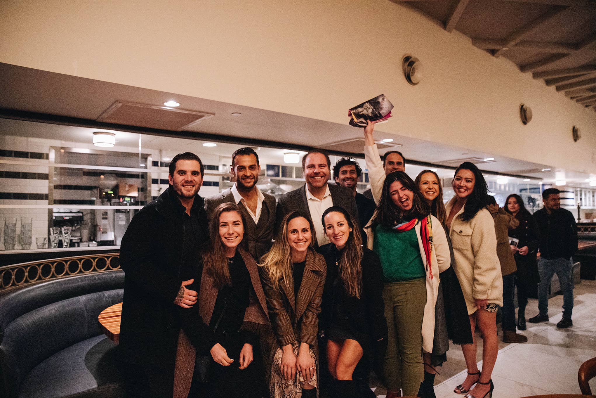 Group of smiling coworkers in a bright office lounge, one person tossing a hat above their head.