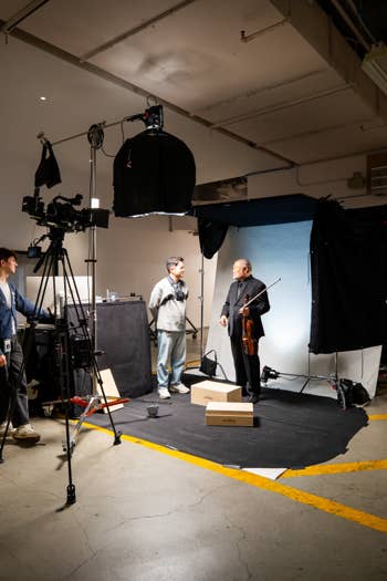 Film studio scene with crew and musicians under large softbox lighting and camera rigs in a warehouse.