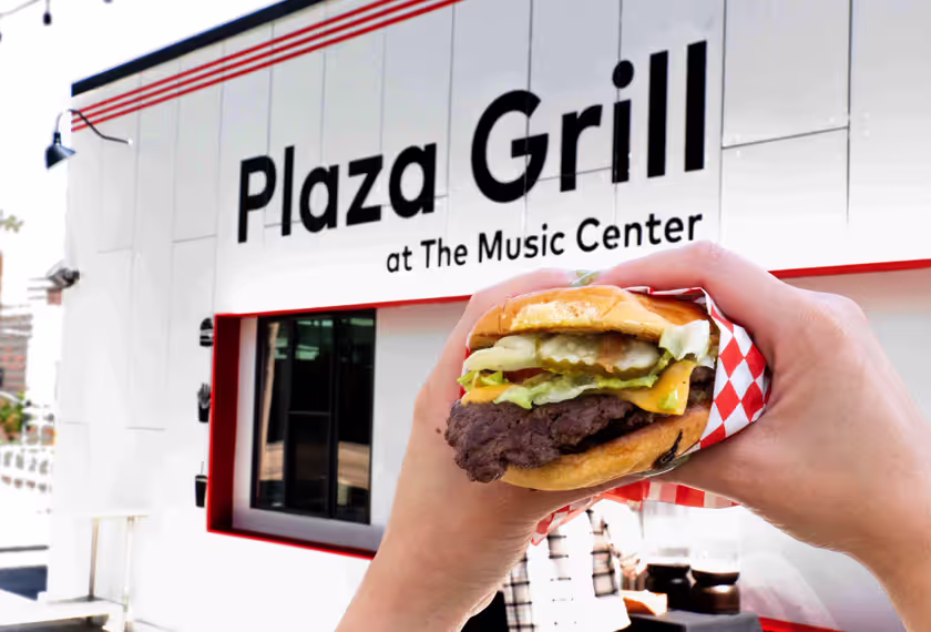 person holding a cheeseburger in front of Plaza Grill sign