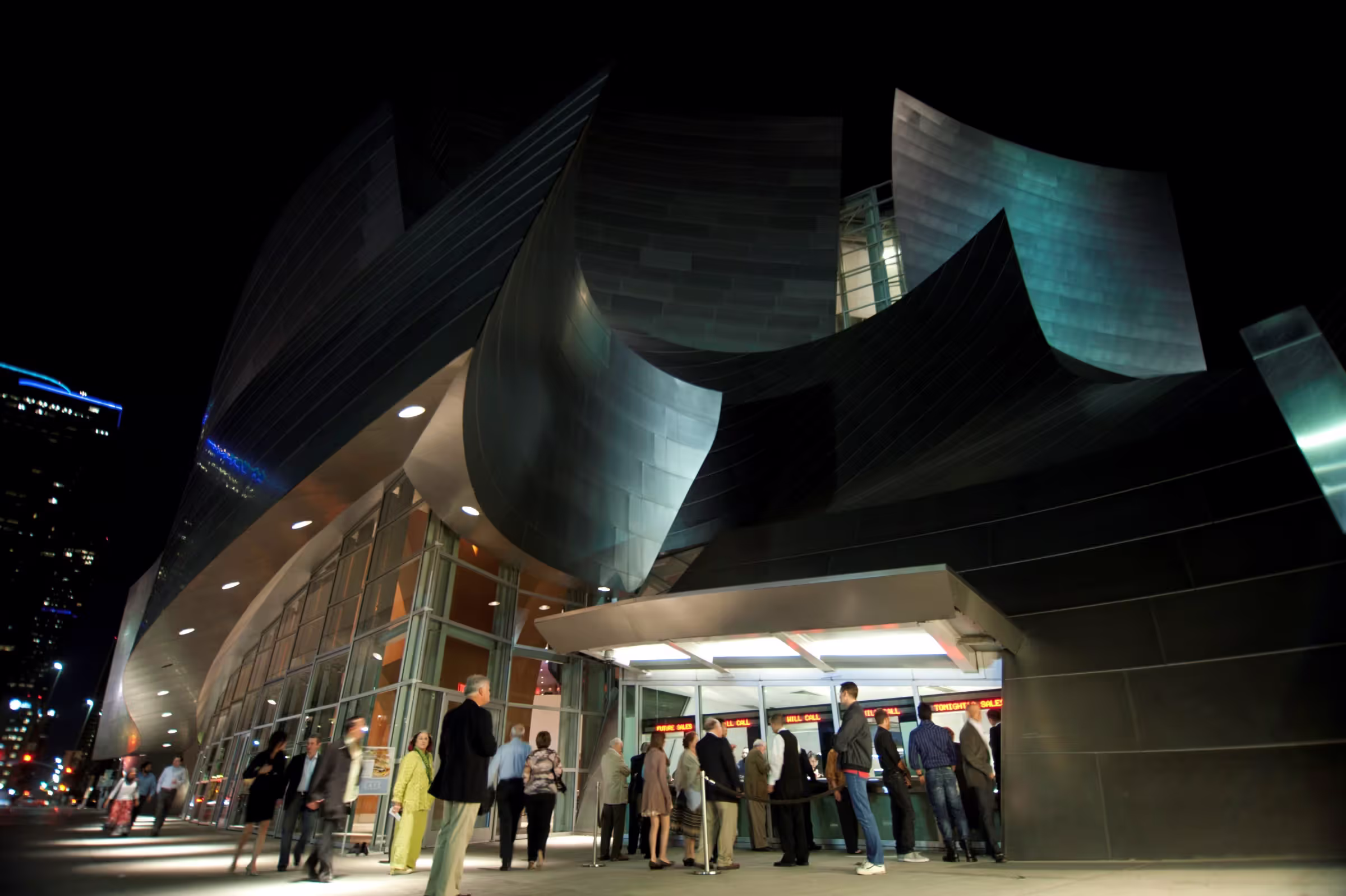 Night view of modern curved glass museum building with people outside and glowing green lights