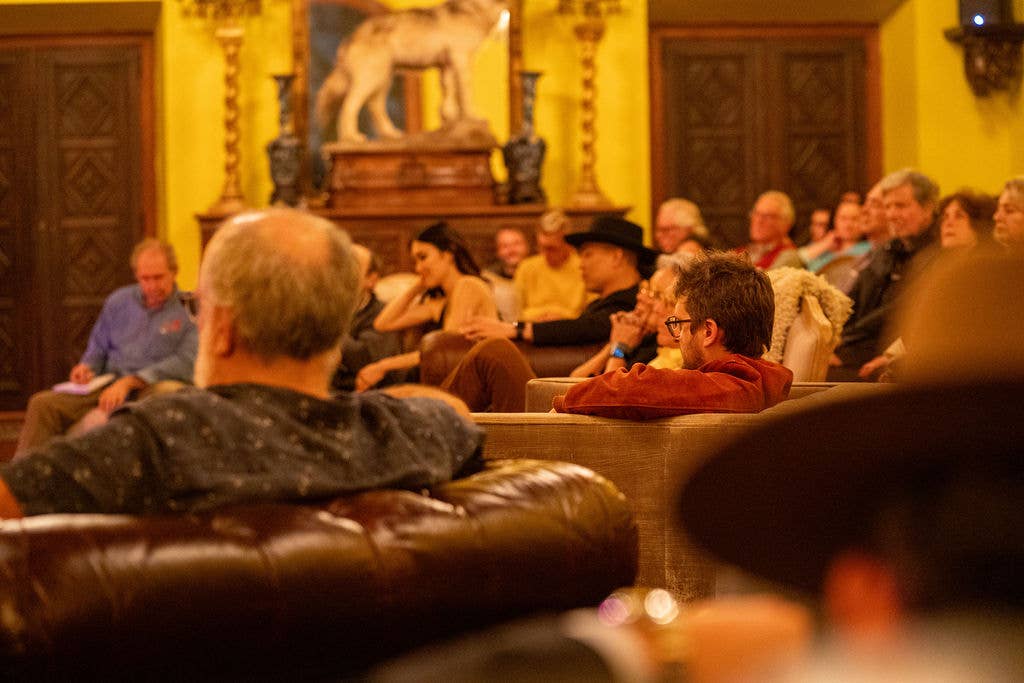 Audience seated in ornate church during a performance, with a musician at the front and rows of listeners