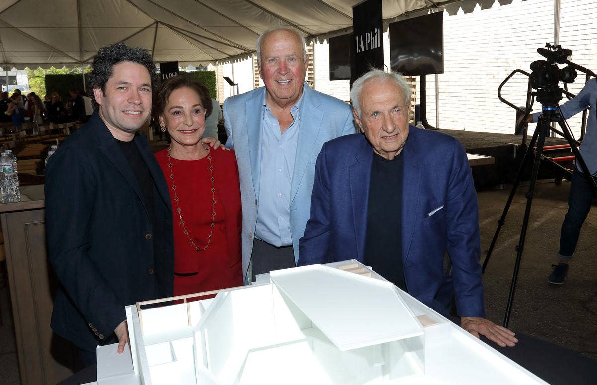 Four people pose at an outdoor event with a photographer setup behind them, beside a white display table.