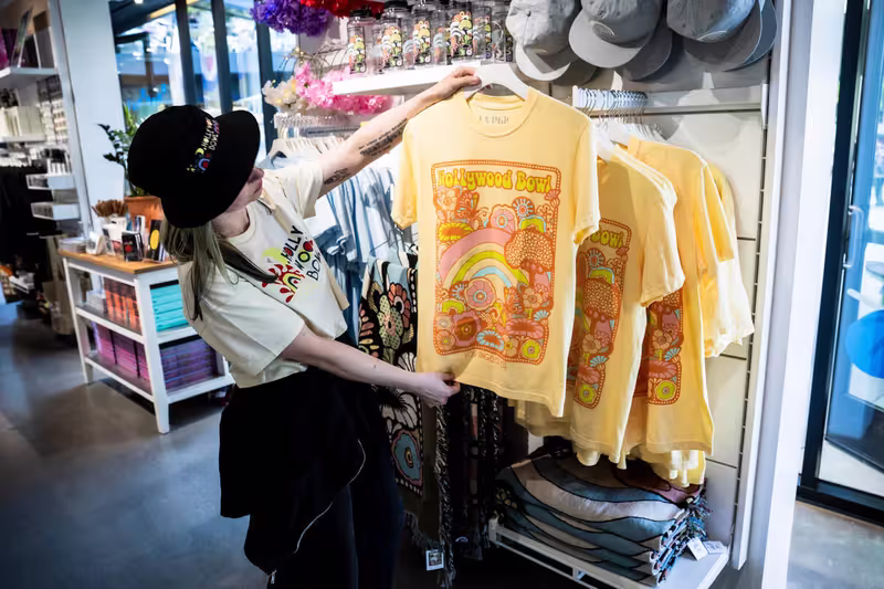 Shopper holds a yellow T-shirt featuring a “Hollywood Bowl” rainbow graphic in a clothing store display.