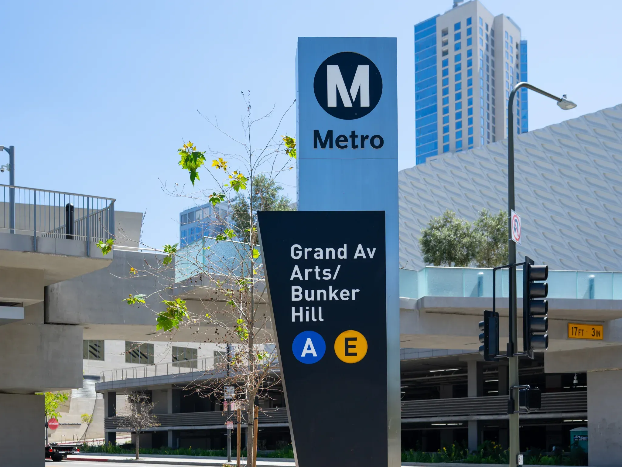 Metro station sign reading Grand Av Arts/Bunker Hill with buildings under a clear blue sky