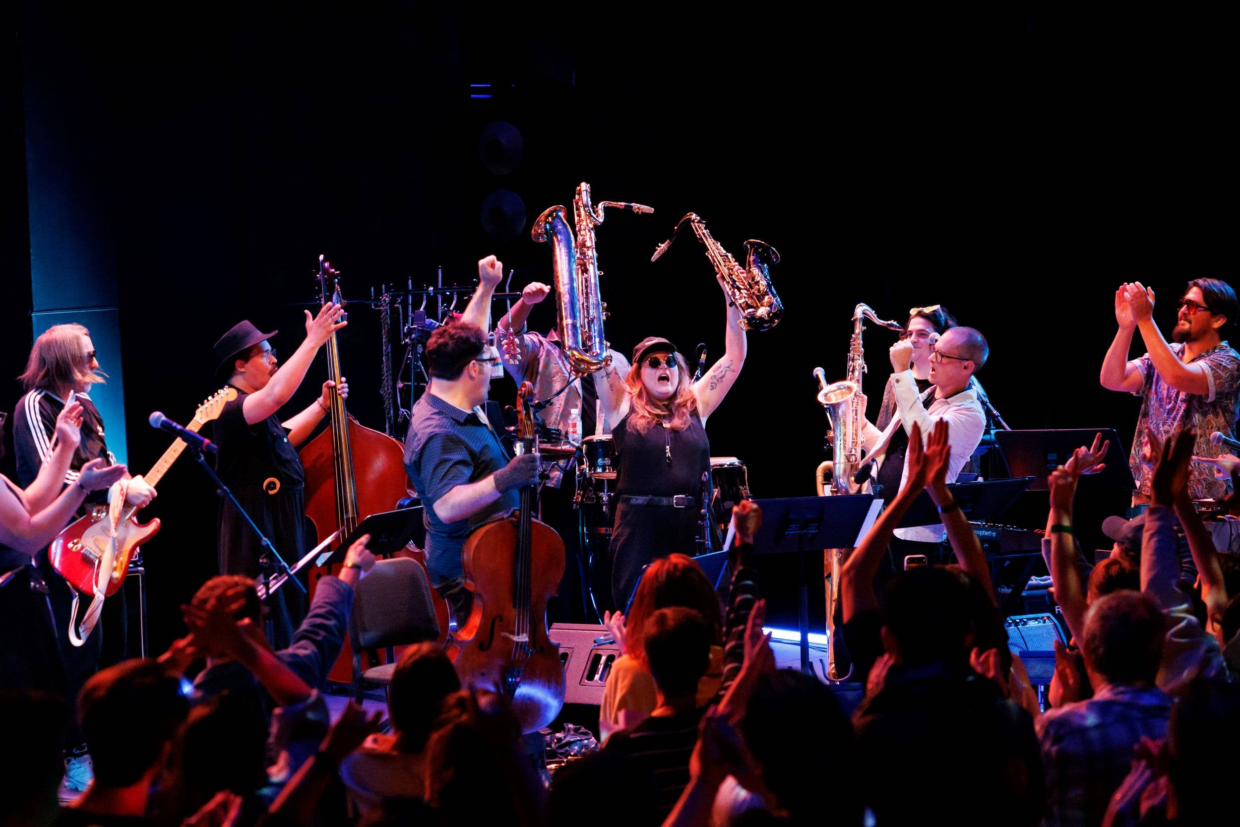 Band performing on stage with saxophones, guitars, and drums as a vocalist sings to an applauding crowd