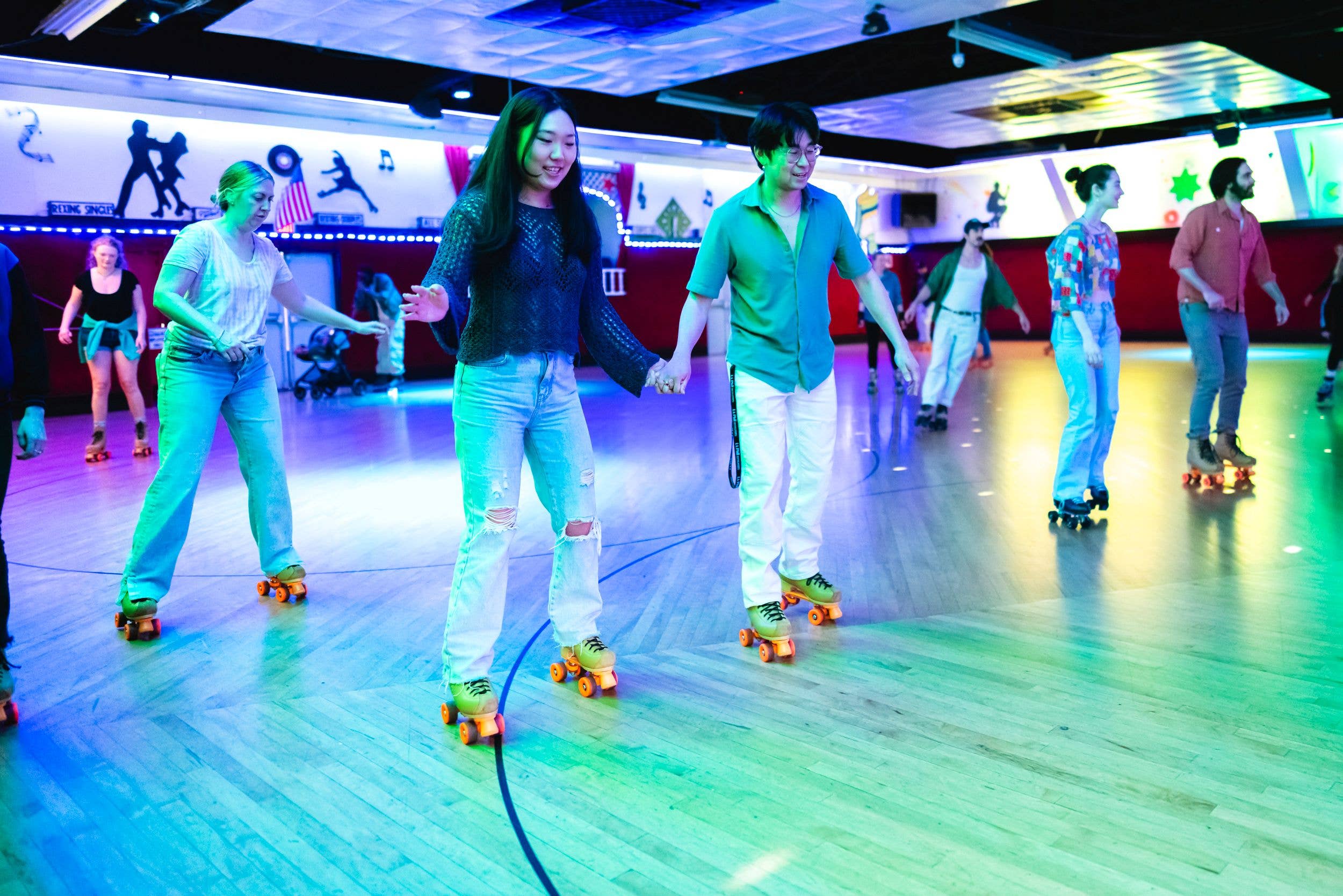 Group roller skating in a brightly lit indoor rink with colorful neon lighting and roller blades