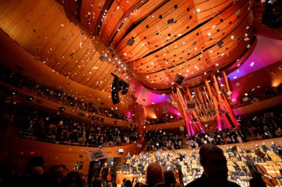 Concert hall interior with orange lighting, musicians on stage, and confetti falling over an audience.
