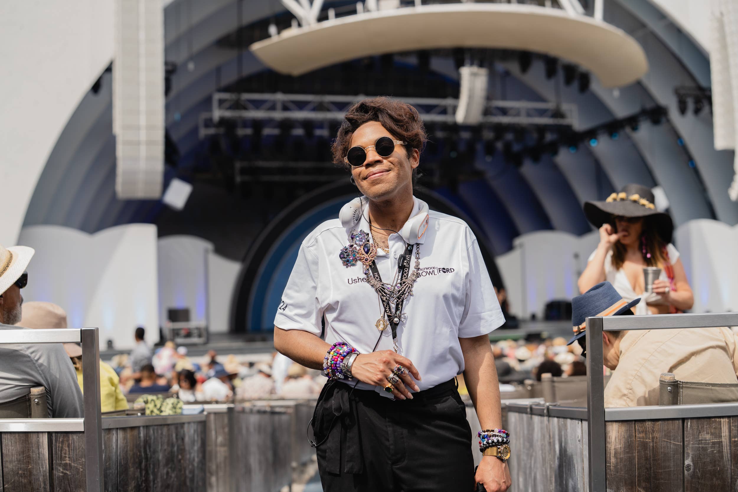 Smiling usher wearing round sunglasses, chains, and a badge at the Hollywood Bowl