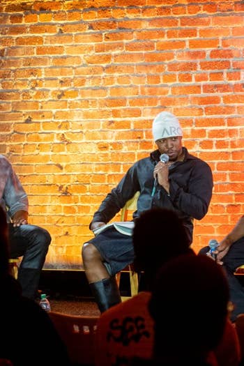 3 performers seated in front of a brick wall giving a talk on stage