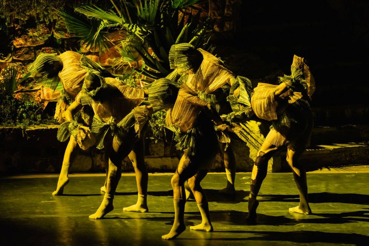 Dancers in yellow fringe costumes perform in a line on a dark stage under green lighting.
