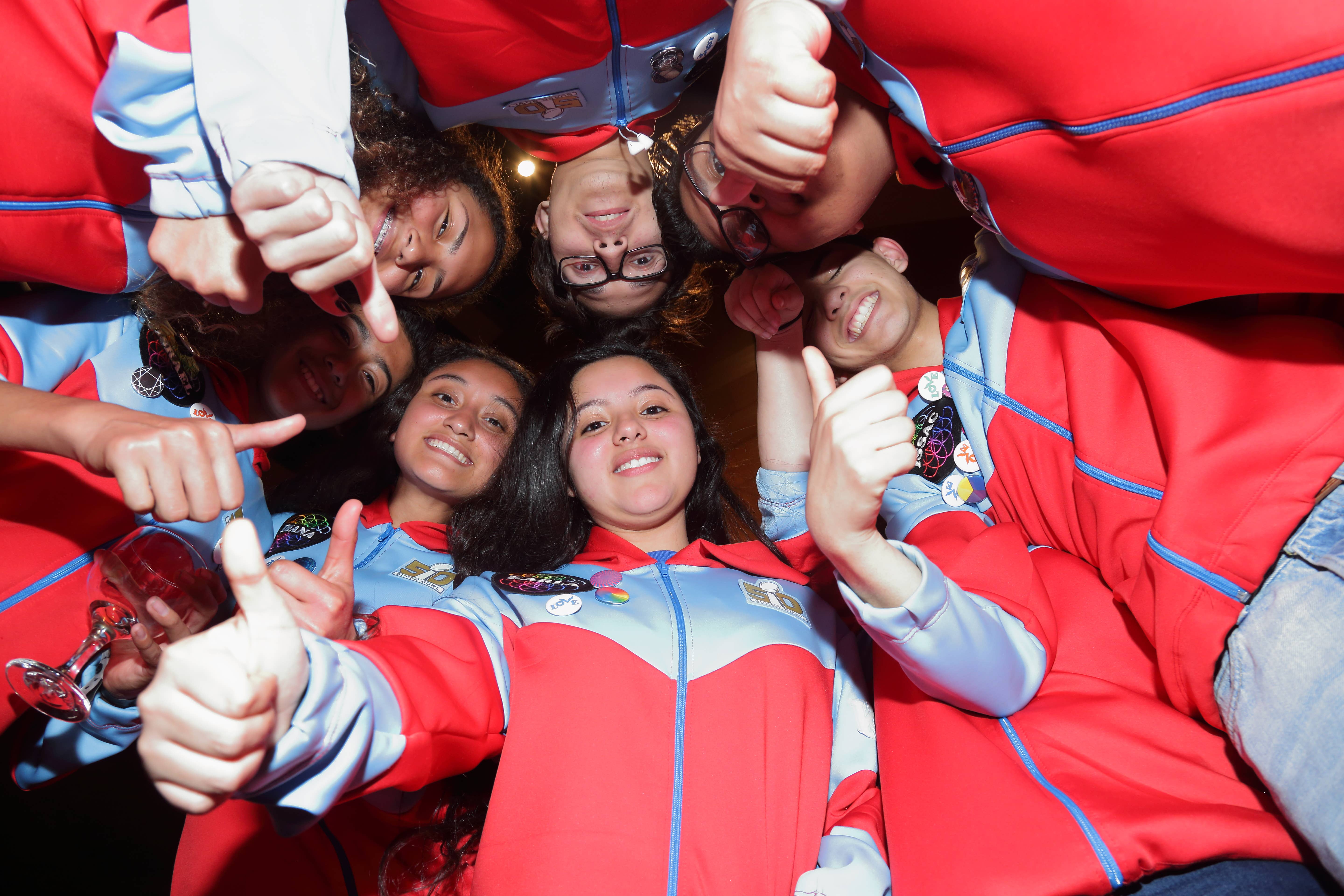 Group of friends in red-and-blue tracksuits posing together, making hand gestures and smiling at the camera.