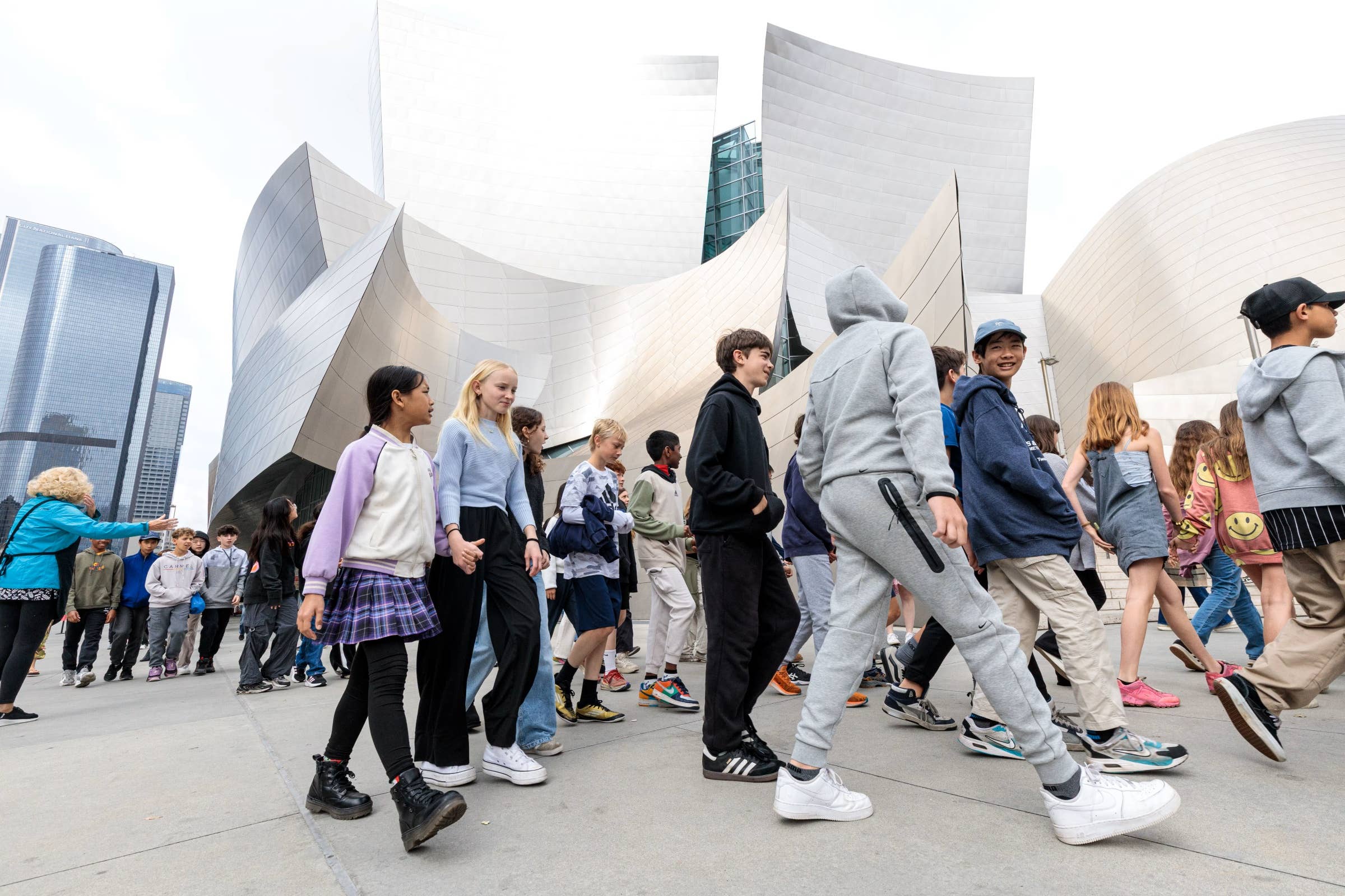 Group of students walking past modern white buildings with curved facades and large city skyscrapers in the background