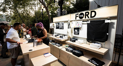 Outdoor booth featuring The FORD merchandise display and customers browsing.