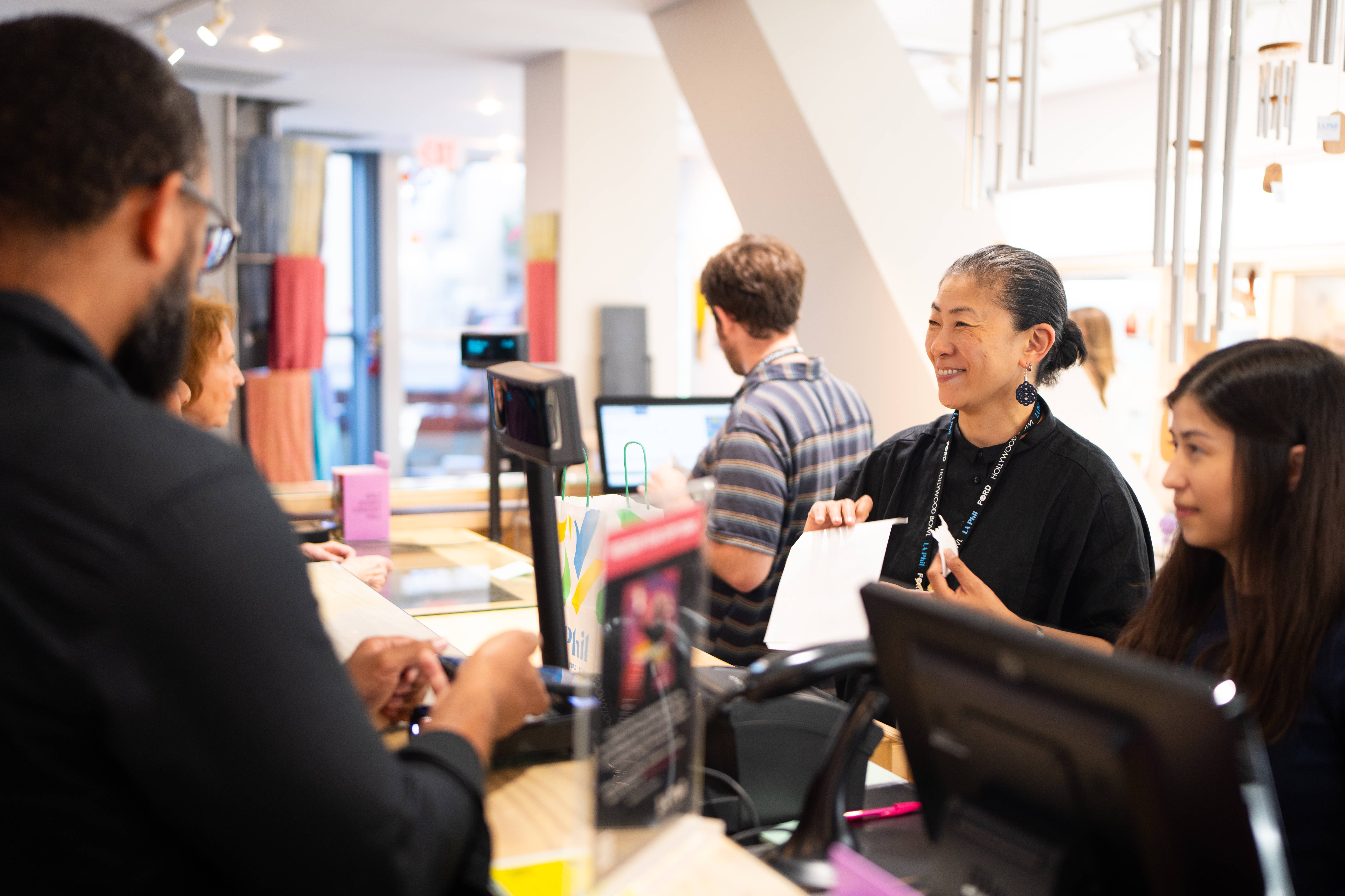 People at a service counter in a bright office, smiling as they talk and exchange documents.