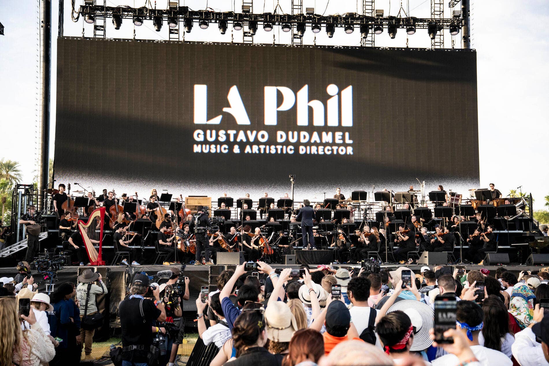 Outdoor concert stage with orchestra musicians and backdrop reading LA Phil and Gustavo Dudamel Music & Artistic Director