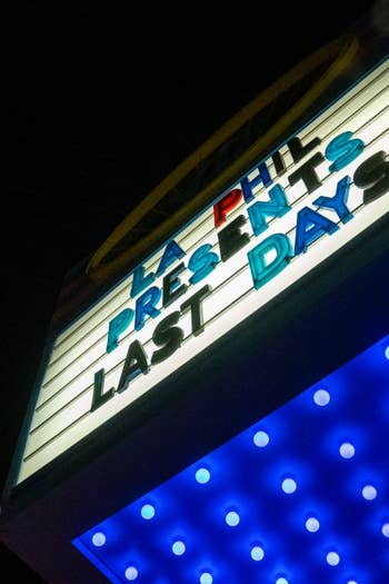 Neon sign reading “LA PHIL PRESENTS LAST DAYS” on a storefront with blue dotted lights at night.